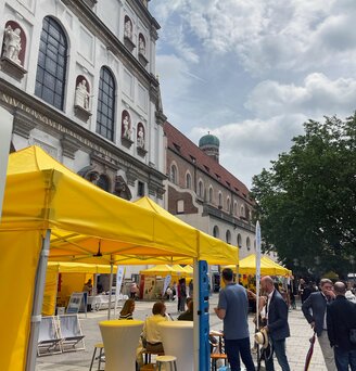 In a shopping street in Munich, there are several yellow folding gazebos from Ecotent's E1/E2 series in the 3x3 size with side walls.